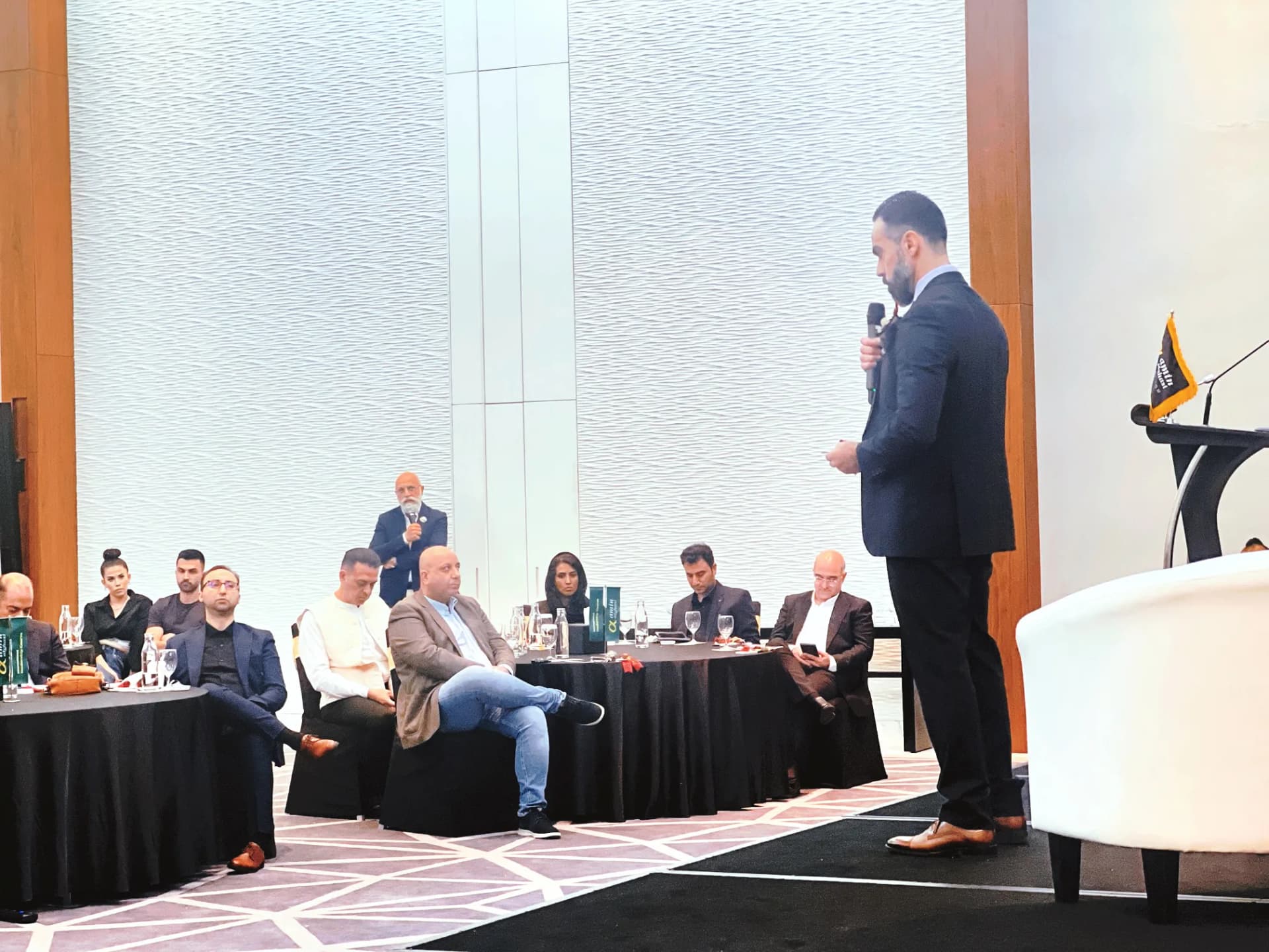 A speaker addressing a seated panel and audience at an NLA leadership event