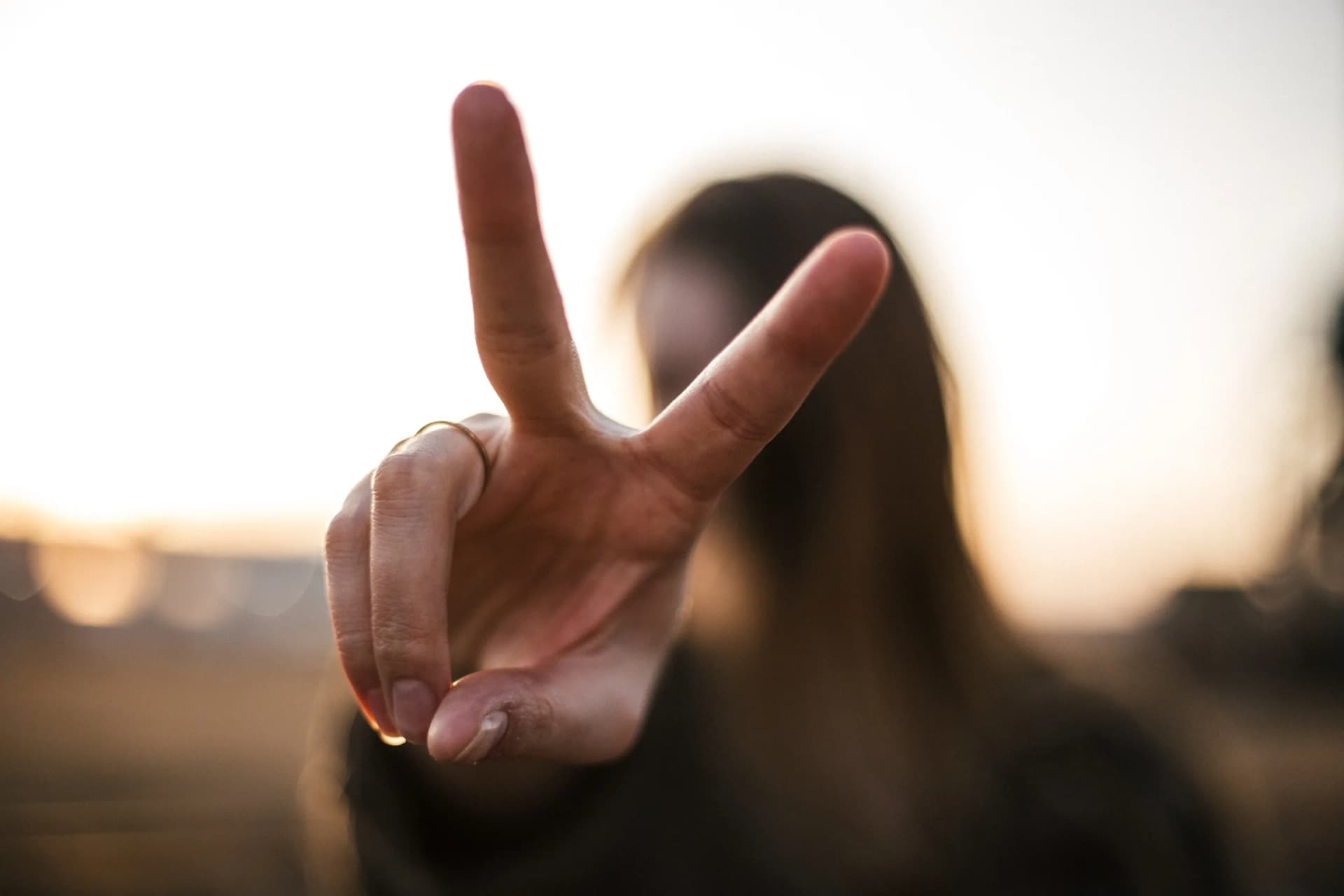 A raised hand held up against a bright sunset, fingers apart