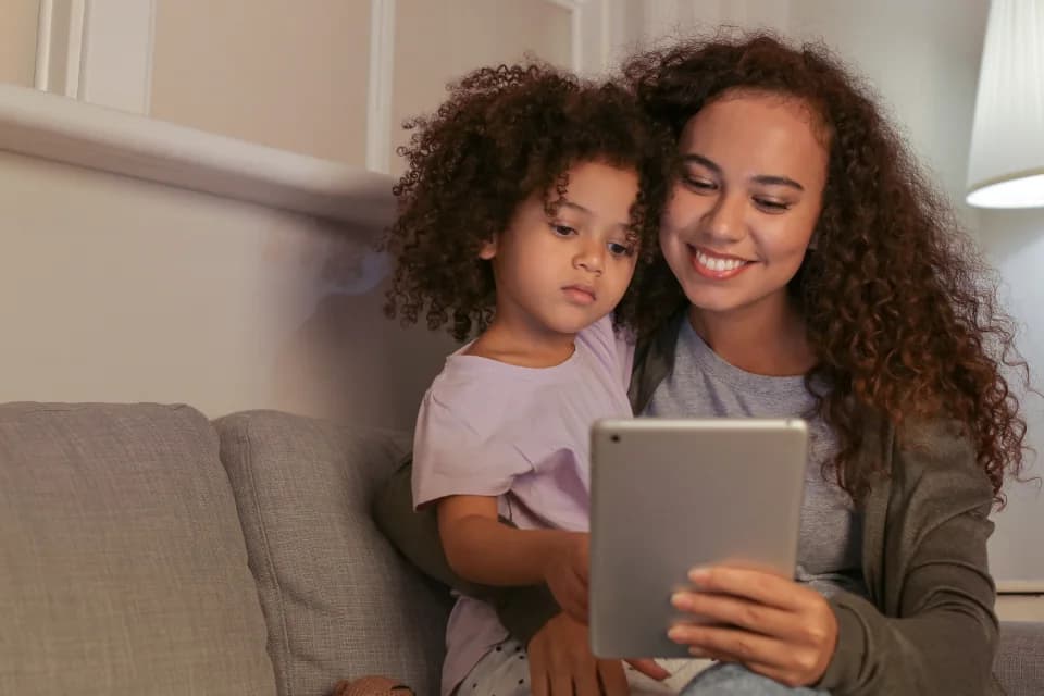A grown-up and a child sitting together on a sofa, reading from a tablet